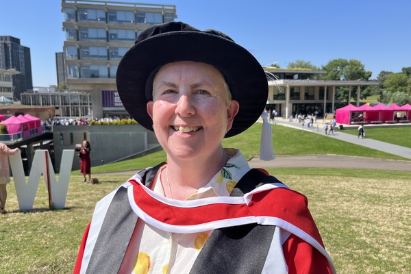 A photo of Jo Todd wearing the formal cap and gown of an academic doctor and smiling outside Essex University.