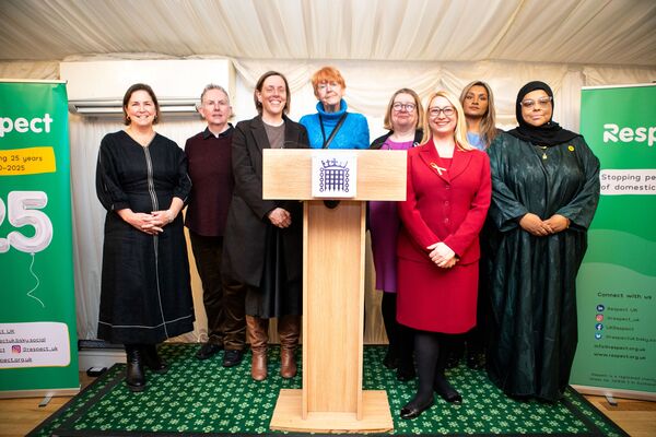 A photo of a group of women standing on a stage at Respect's 25th anniversary event. They are Dame Nicole Jacobs, Jo Todd CBE, Jess Phillips MP, Dame Vera Baird DBE KC, Katrina Murray MP, Jess Asato MP, Shana Begum and Annie Gibbs. 
