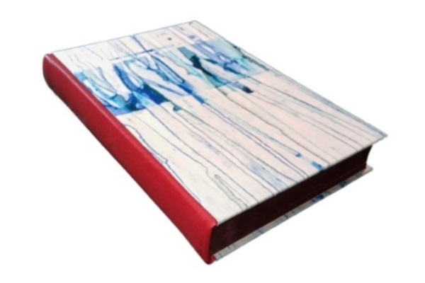 Photo of a binding with a red leather spine and white boards with a blue dripped design, with the boards laid on top of the spine leather.