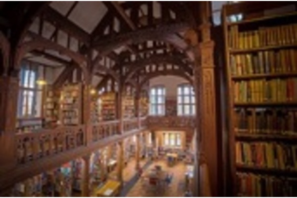 Photo of the interior of Gladstone Library, with a vaulted timber roof and bookcases lining the walls. The photo is taken from a balcony, and sunlight shines through the windows.