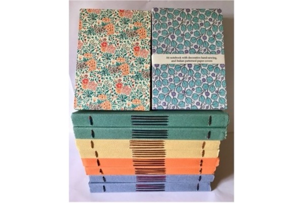 Photo of a stack of bindings with brightly-coloured solid spines and decorative paper sides. The spines have exposed kettle stitches and a longstitch panel in the centre.