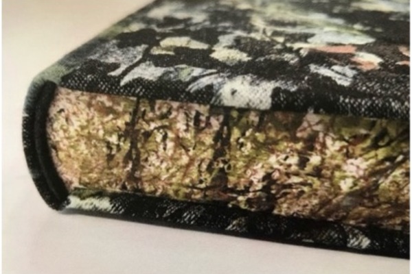 Close-up off the tail of a book with a black, purple, and green sponged pattern on the cloth, and a similar pattern on the textblock.