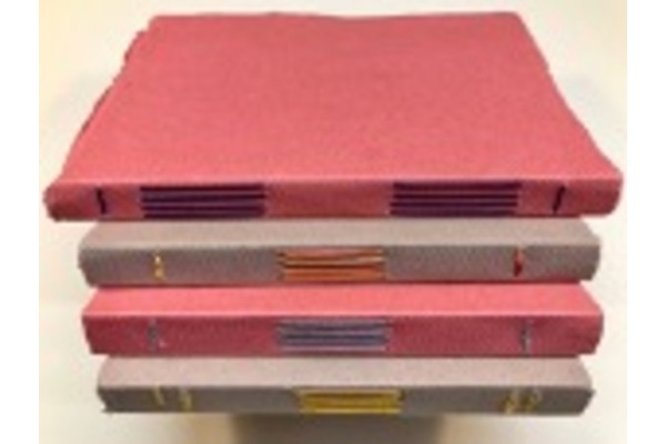 Photo of a stack of thick paper longstitch bindings with brightly-coloured thread