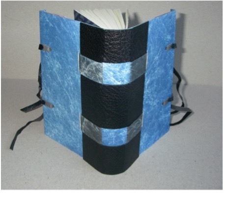 Photo of the spine of a book with splayed boards, quarter black leather with light blue sides and black ribbon ties, with two light blue strips crossing the spine.