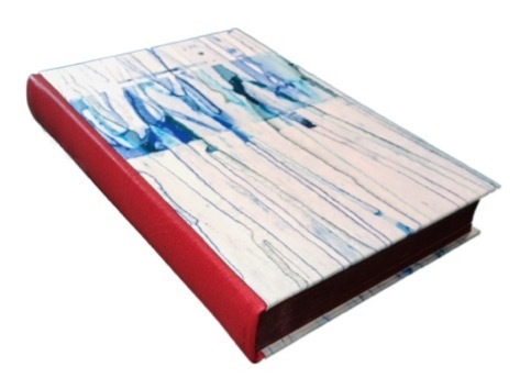 Photo of a binding with a red spine and white boards with a blue dripped pattern. The boards are placed on top of the spine leather.