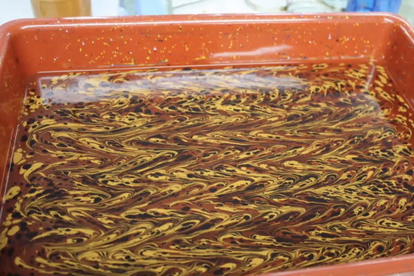 A photo of a tray with a red, yellow, and black marbled comb pattern floating at the top