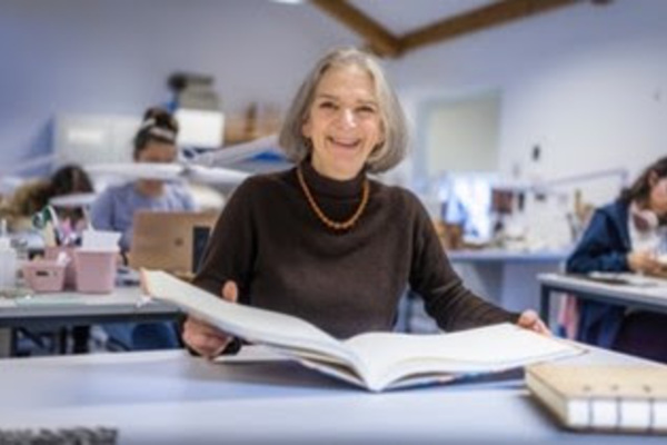 Lizzie Neville smiling and holding a book in her studio