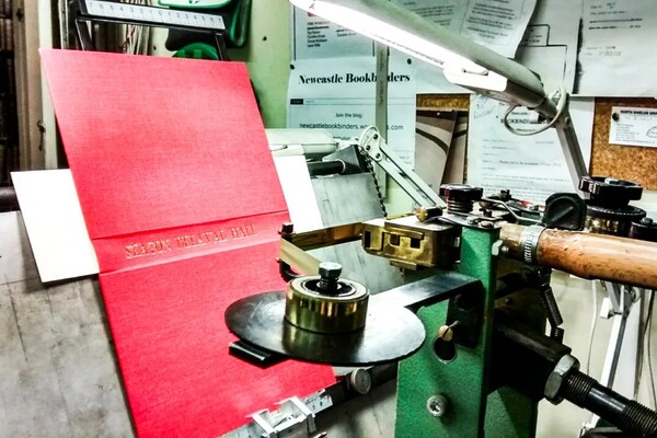A cloth book cover being stamped by a foil lettering machine