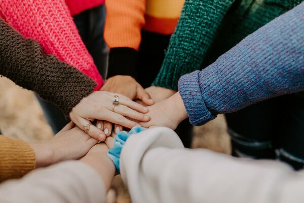 A group of people with different coloured clothes connect hands in the centre of the image showing solidarity, diversity and togetherness.