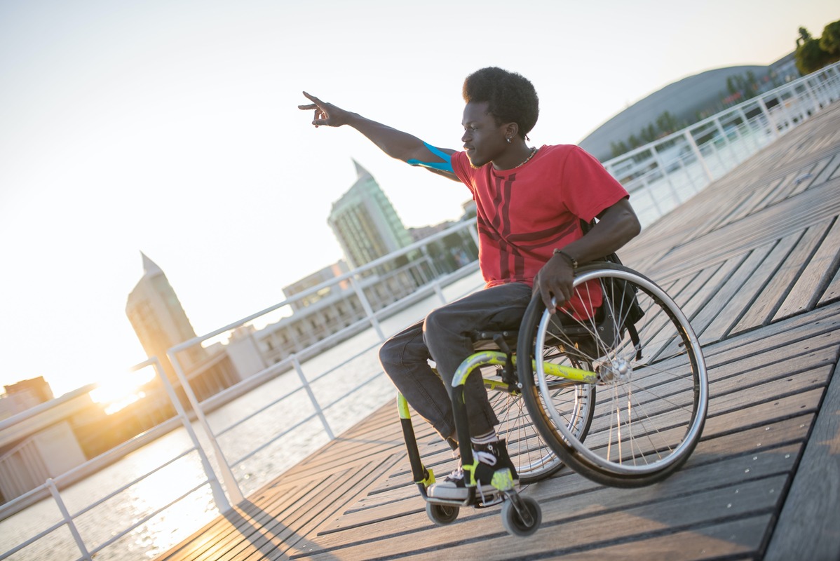 Black man sitting in wheelchair on pier at sunset. 