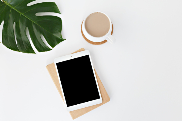Overhead view of iPad, coffee and monstera leaf on a desk